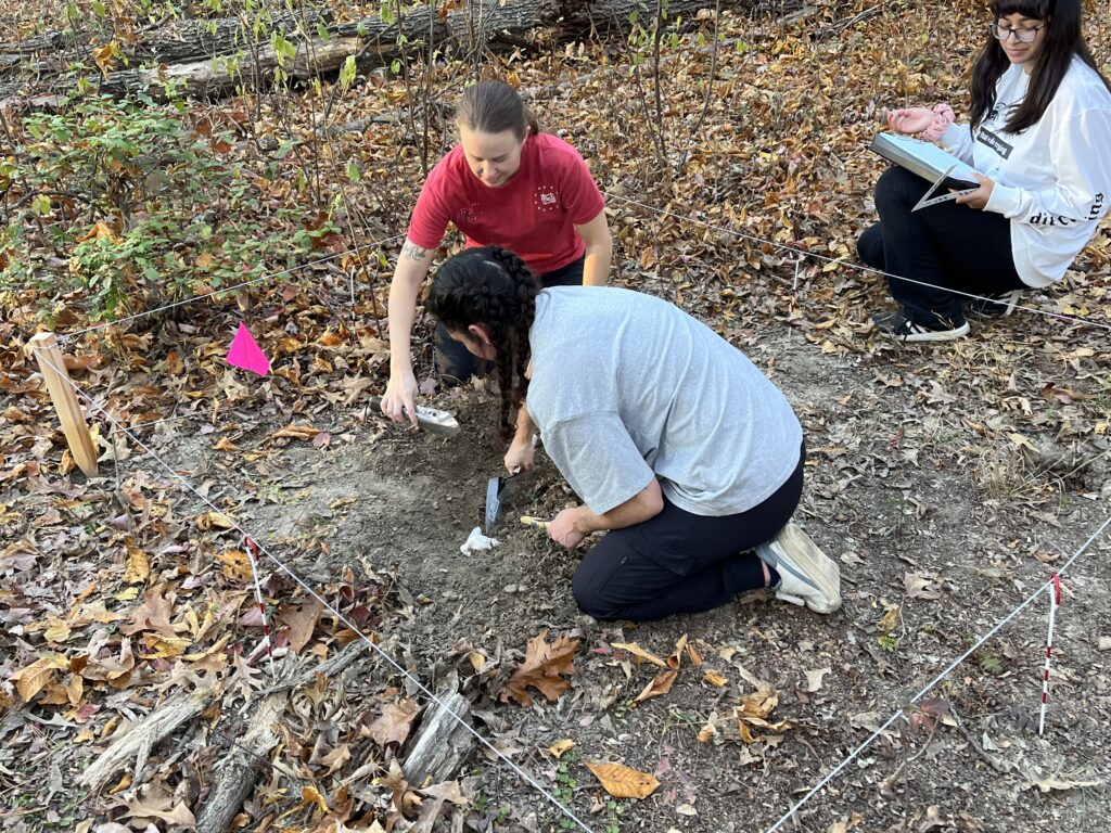 Students digging away skeletal remains at a body research site.
